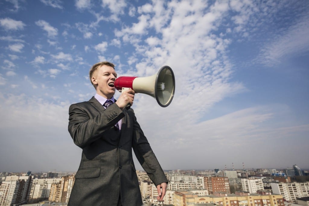 young businessman in suit screaming into megaphone on the roof